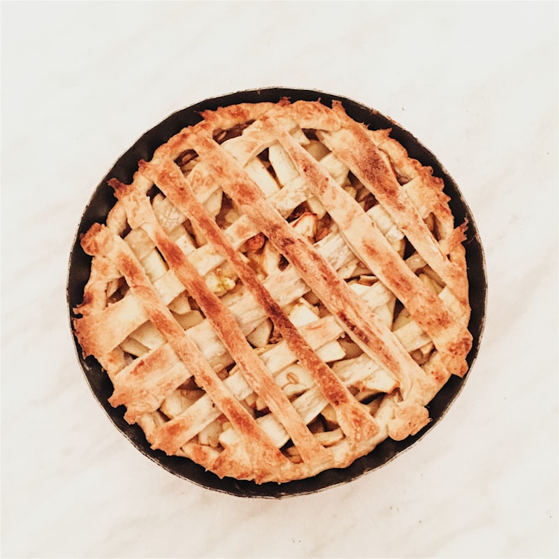 Golden-brown fruit pie with decorative flaky lattice crust cooling on marble kitchen counter